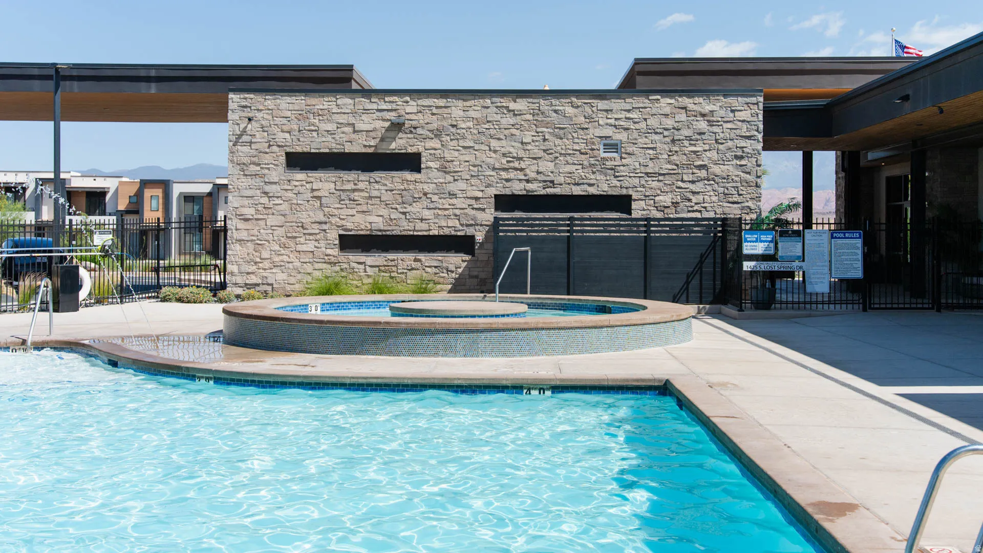Outdoor swimming pool featuring a connected circular spa, surrounding concrete decking, and contemporary stone-clad building