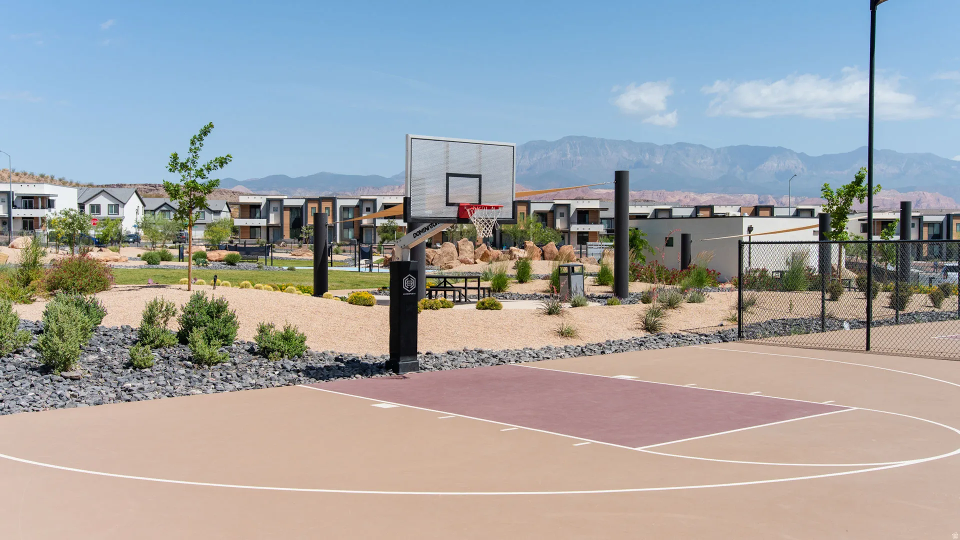 Outdoor half-basketball court with a tan and maroon playing surface, white court lines, and a black basketball hoop