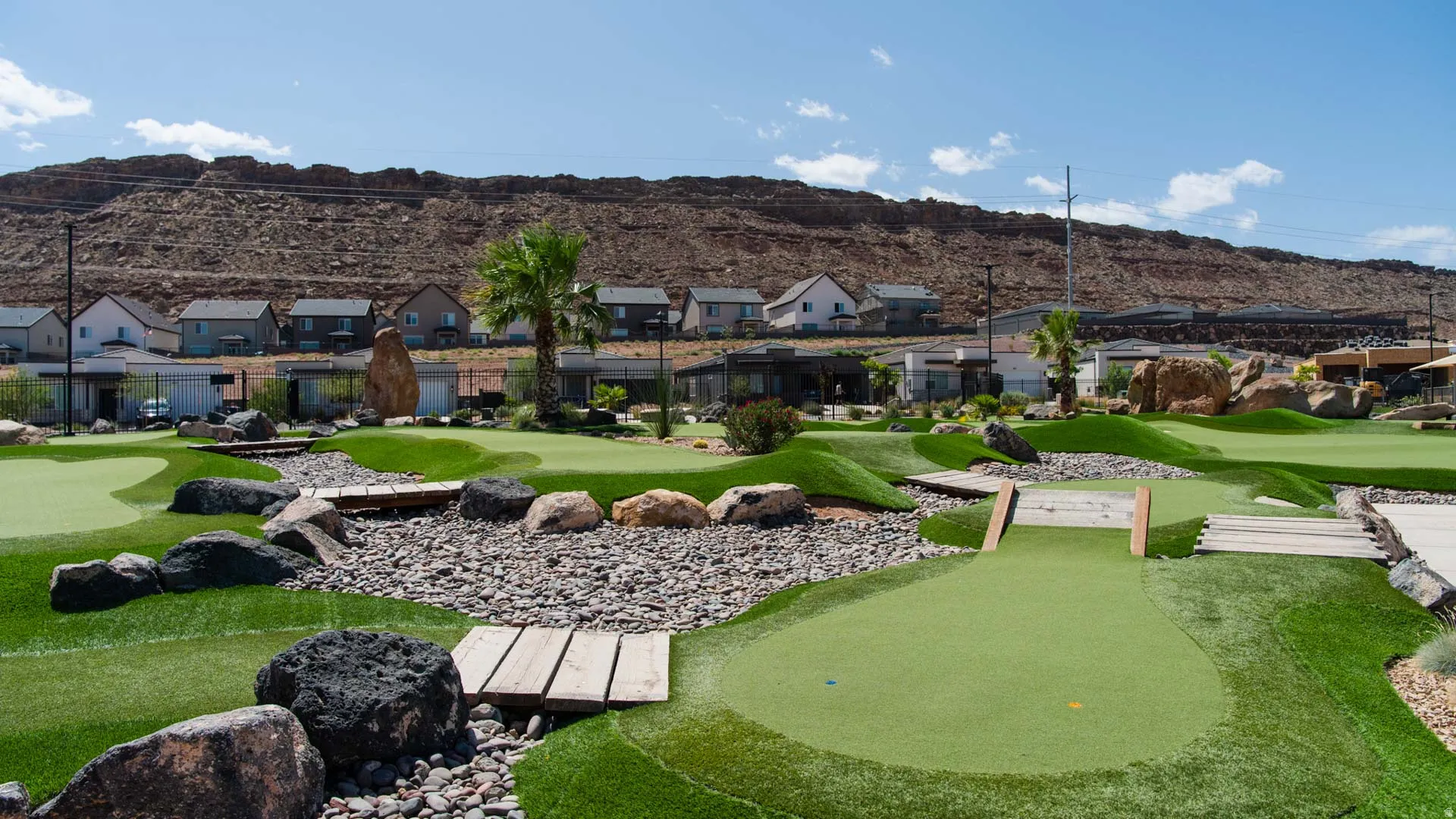 Expansive putting green area featuring artificial turf, decorative rock landscaping, and multiple wooden footbridges