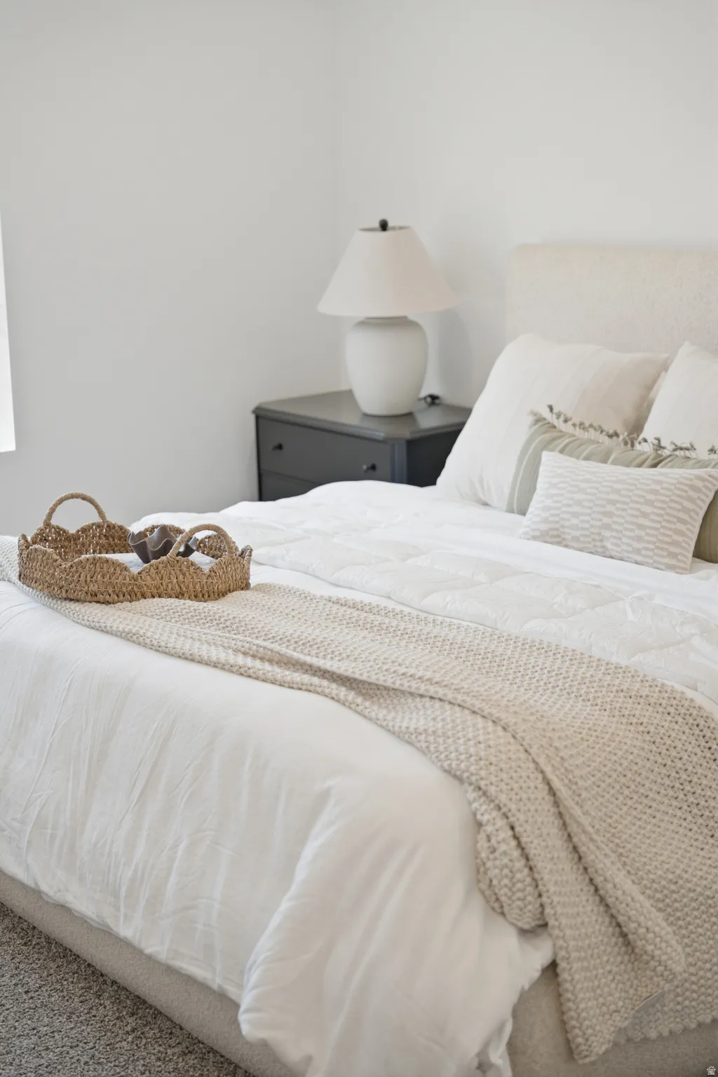 Bedroom featuring an upholstered headboard, clean white walls, and a dark-toned nightstand with a ceramic lamp