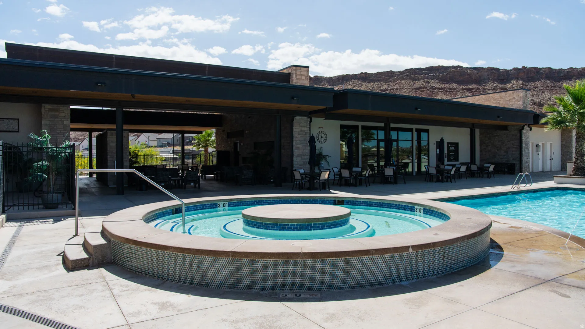 Outdoor pool area featuring a circular spa with mosaic tiling, an adjacent swimming pool, and concrete decking