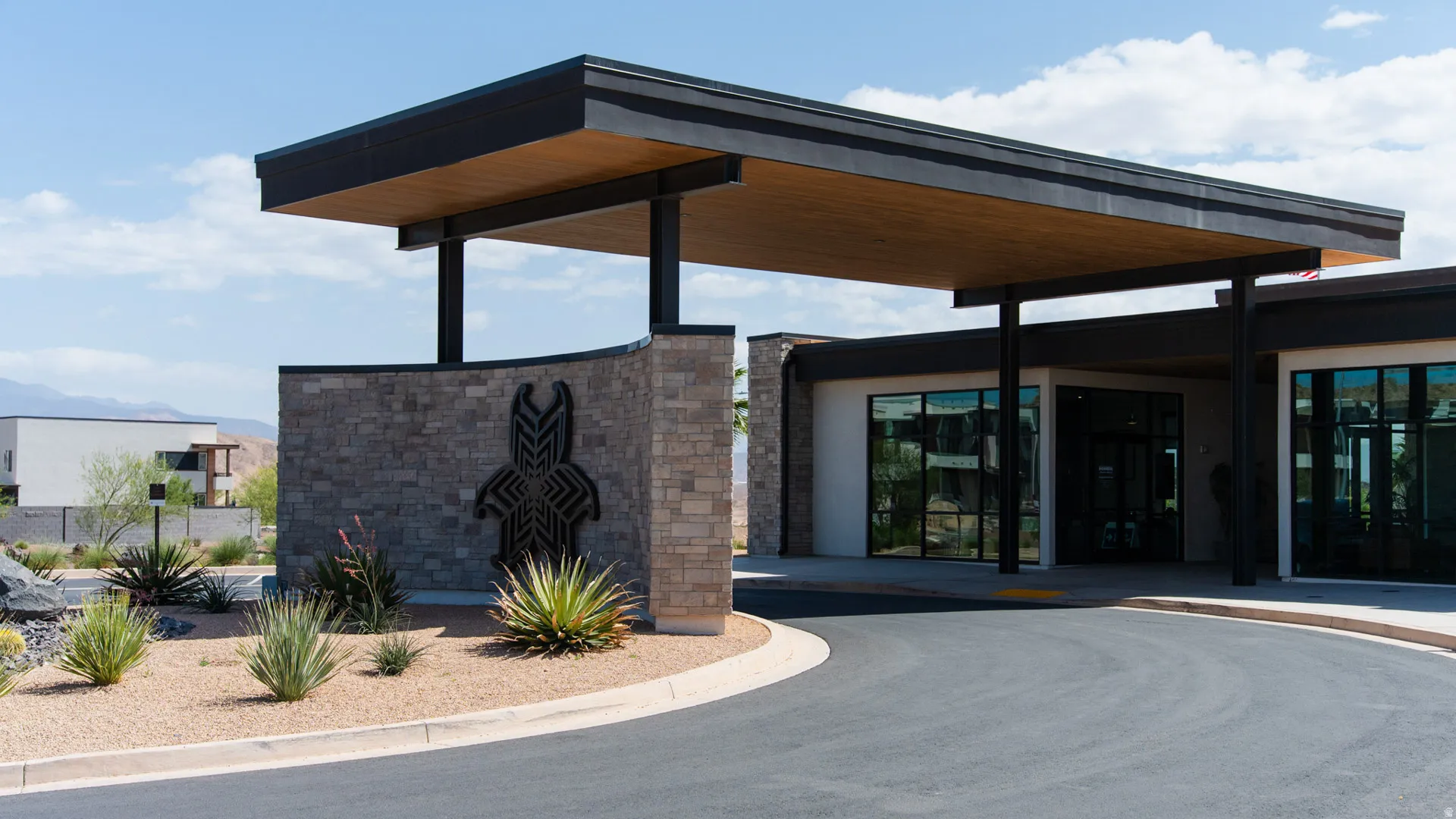 Contemporary porte-cochere entrance featuring a wood-finish ceiling, stone veneer accents, and a distinctive metal art piece