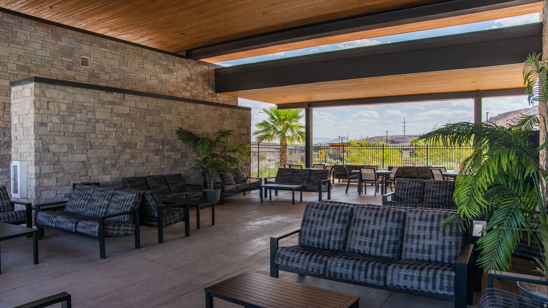 Expansive covered patio featuring exposed wood beam ceiling with integrated lighting, brick accent wall, and concrete flooring