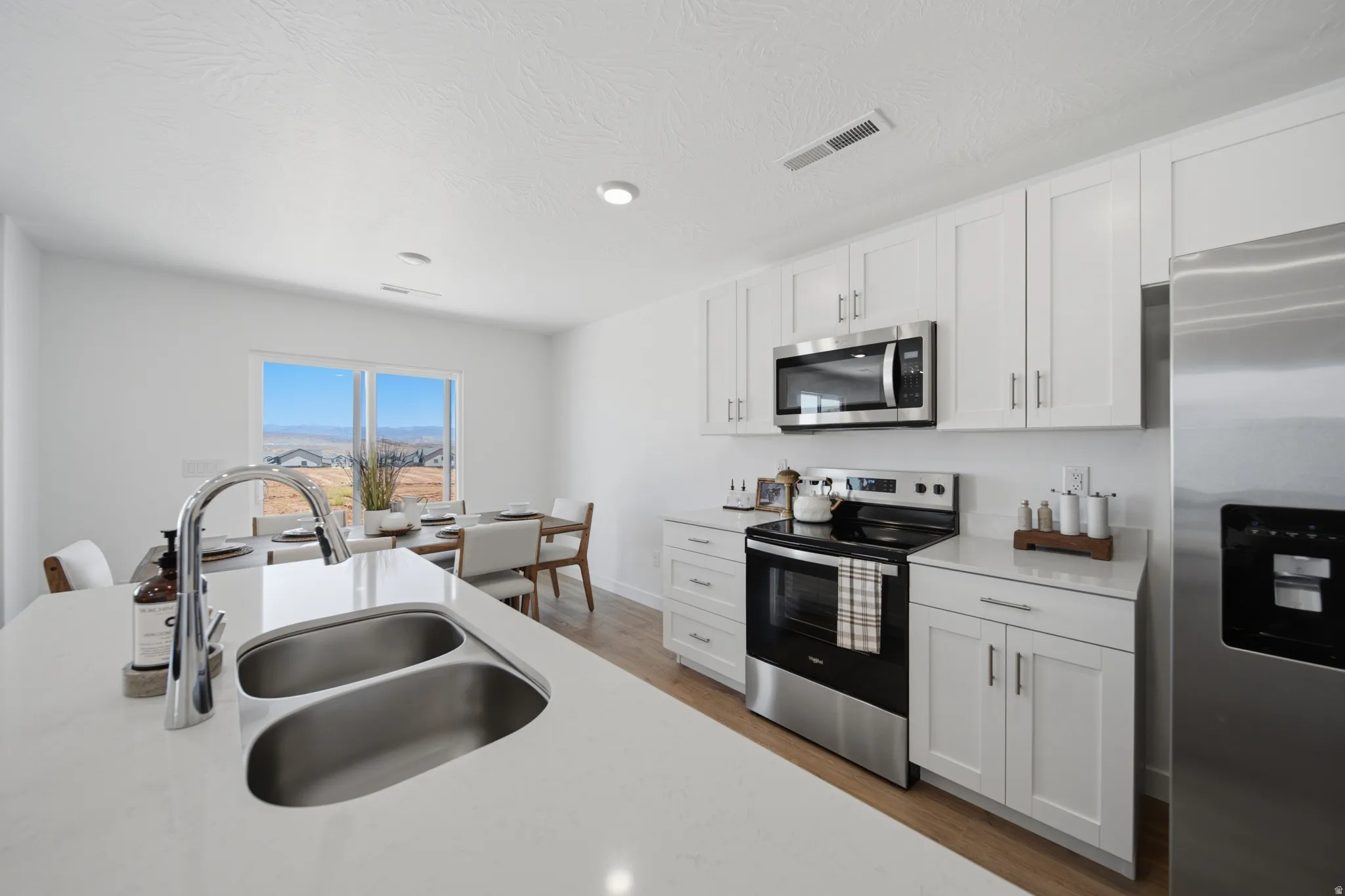 Modern kitchen featuring white shaker cabinetry, stainless steel appliances, a white solid surface countertop, and wood-finish flooring