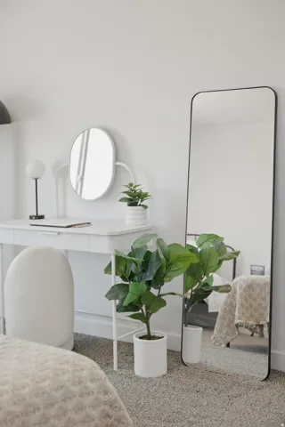 Neutral-toned bedroom featuring wall-to-wall carpeting, a white desk, and a full-length mirror with a black frame