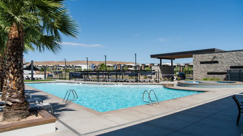 Community swimming pool featuring a connected spa, stone-clad clubhouse, covered lounge area, and desert landscaping