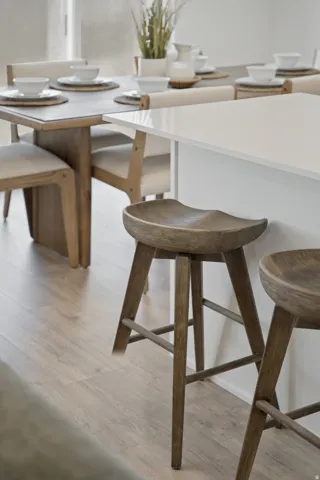 Modern dining space featuring a white quartz countertop island with waterfall edge, natural wood-finish bar seating with sculptural turned-leg stools, and light wood-finish flooring throughout
