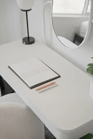 White desk with a curved mirror, spherical light fixture, and plush seating