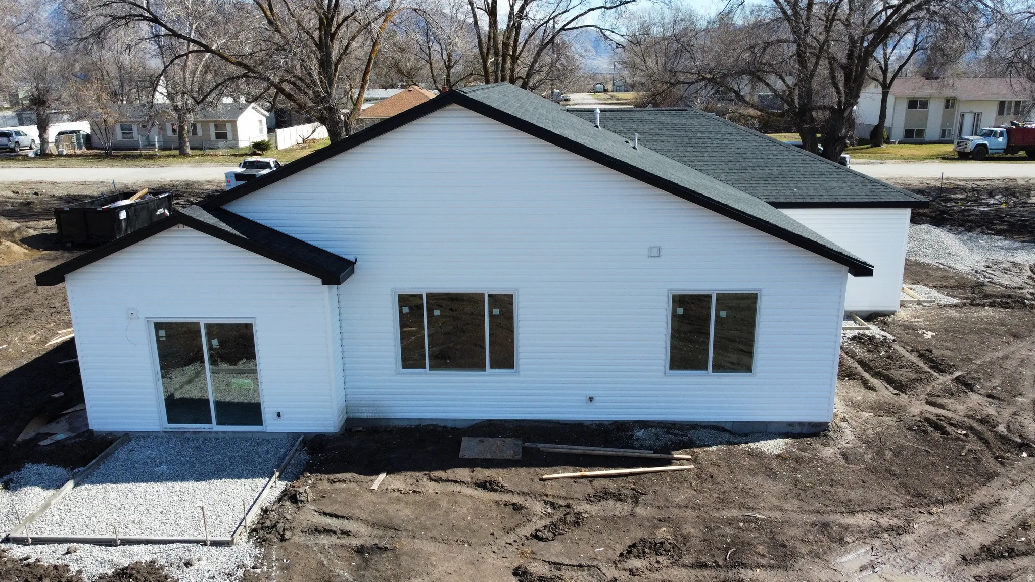 Modern residential construction featuring clean white exterior siding, a pitched roof with dark asphalt shingles, and multiple window openings across the front facade