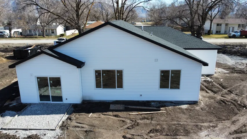 Modern residential construction featuring clean white exterior siding, a pitched roof with dark asphalt shingles, and multiple window openings across the front facade