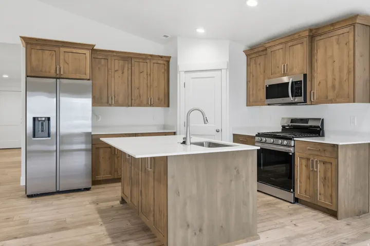 Modern kitchen featuring light wood-finish cabinetry, stainless steel appliances, a center island with a sink, white countertops, and wood-finish flooring
