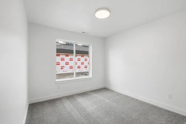 Bright room featuring a window with white trim, gray carpet, white walls, and a flush-mount ceiling light