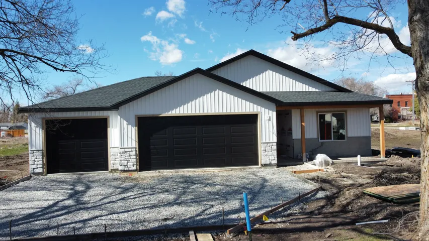 Newly constructed residence featuring vertical siding, stone veneer accents, a dark asphalt shingle roof, and two integrated garage doors