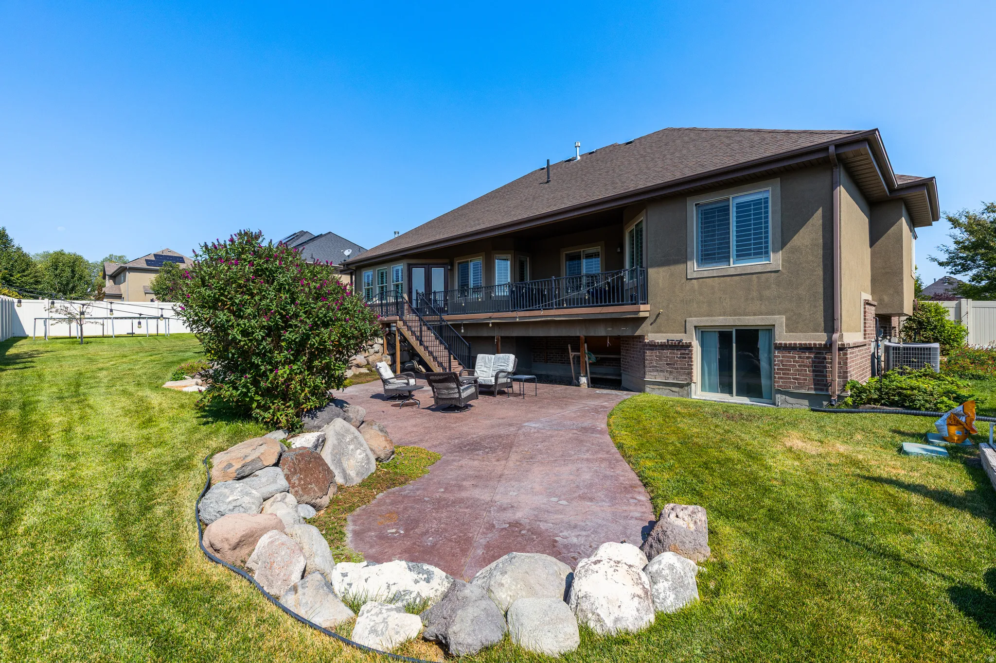 Expansive backyard featuring a large stamped concrete patio, a rock border, and a mature shrub