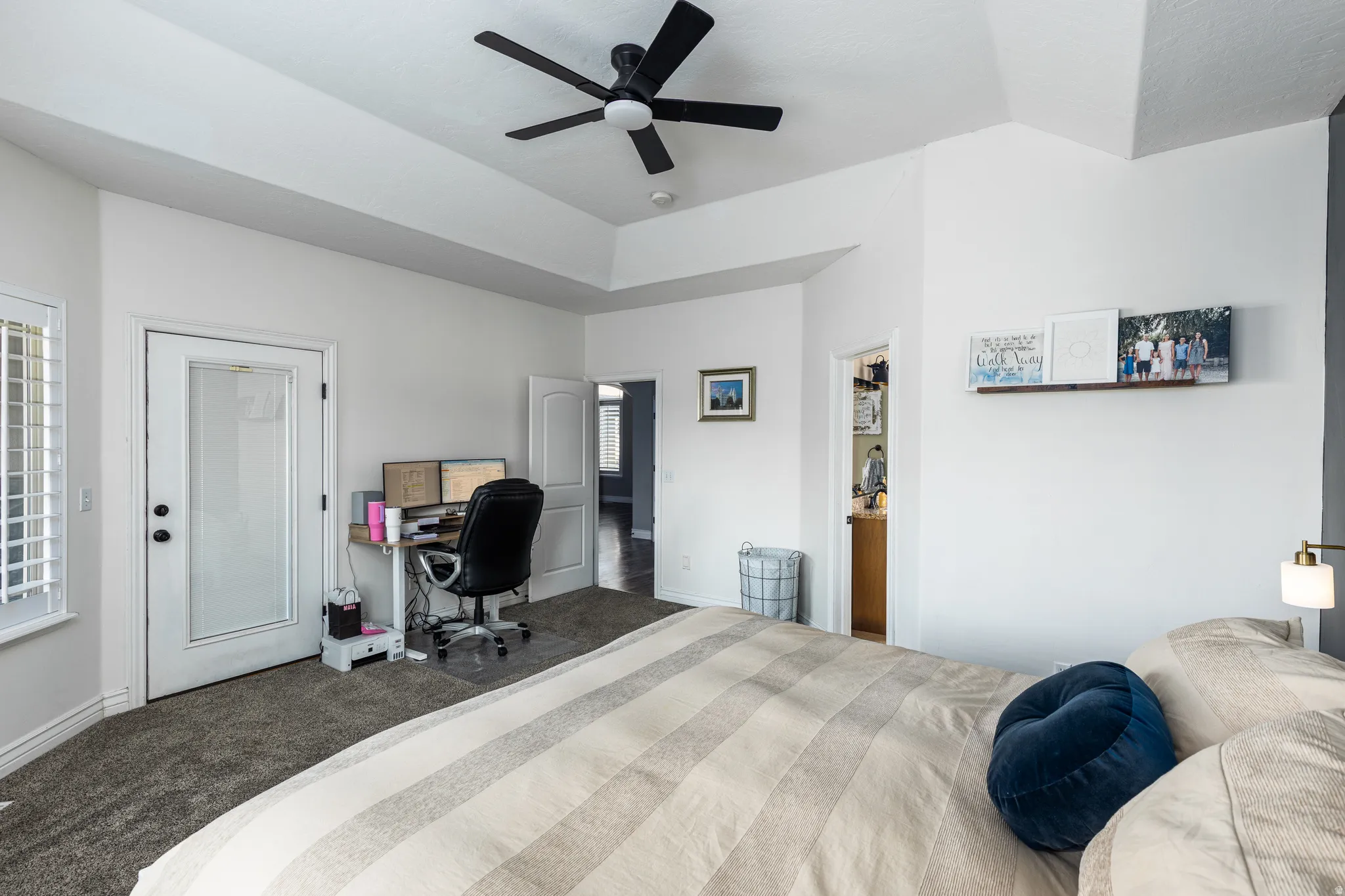Spacious primary bedroom featuring neutral carpeting, a coffered ceiling with integrated ceiling fan, and abundant natural light from multiple windows