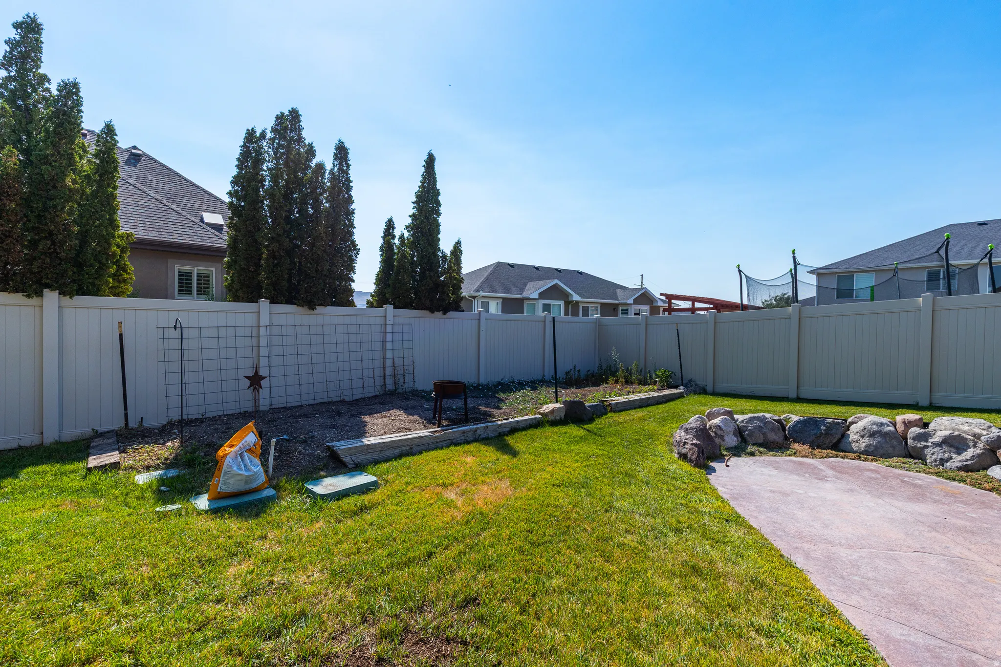 Expansive backyard featuring a manicured lawn, a large concrete patio area, and a stone retaining wall