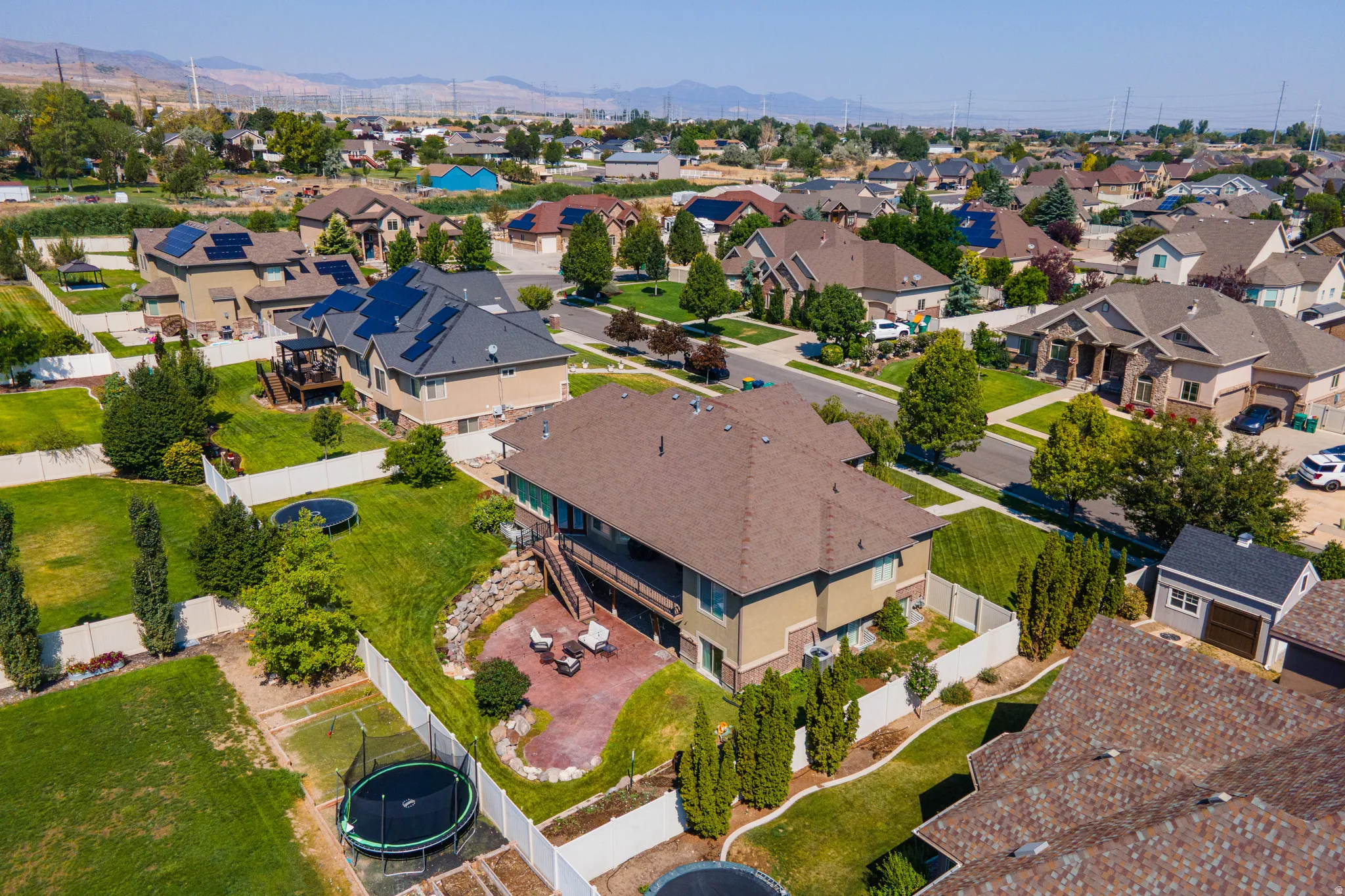 Landscaped backyard featuring a terraced paver patio, a white privacy fence, and mature trees
