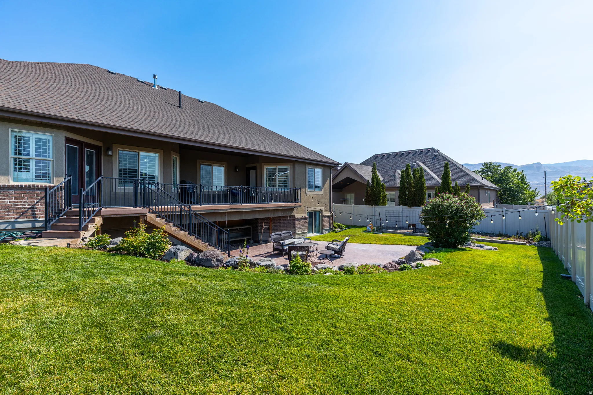 Expansive rear yard featuring a large patio, lush lawn, mature landscaping, and a multi-level deck with black railings