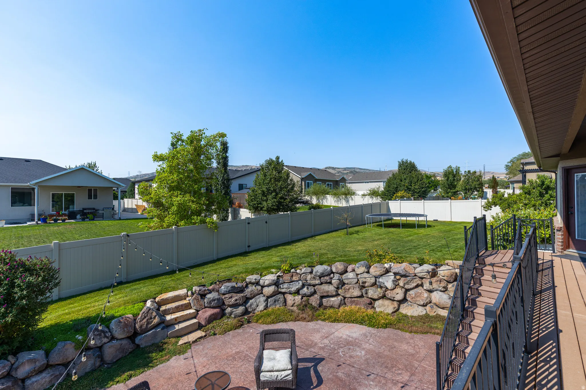 Terraced backyard featuring a spacious composite deck with black metal railings, a concrete patio, and natural stone retaining walls