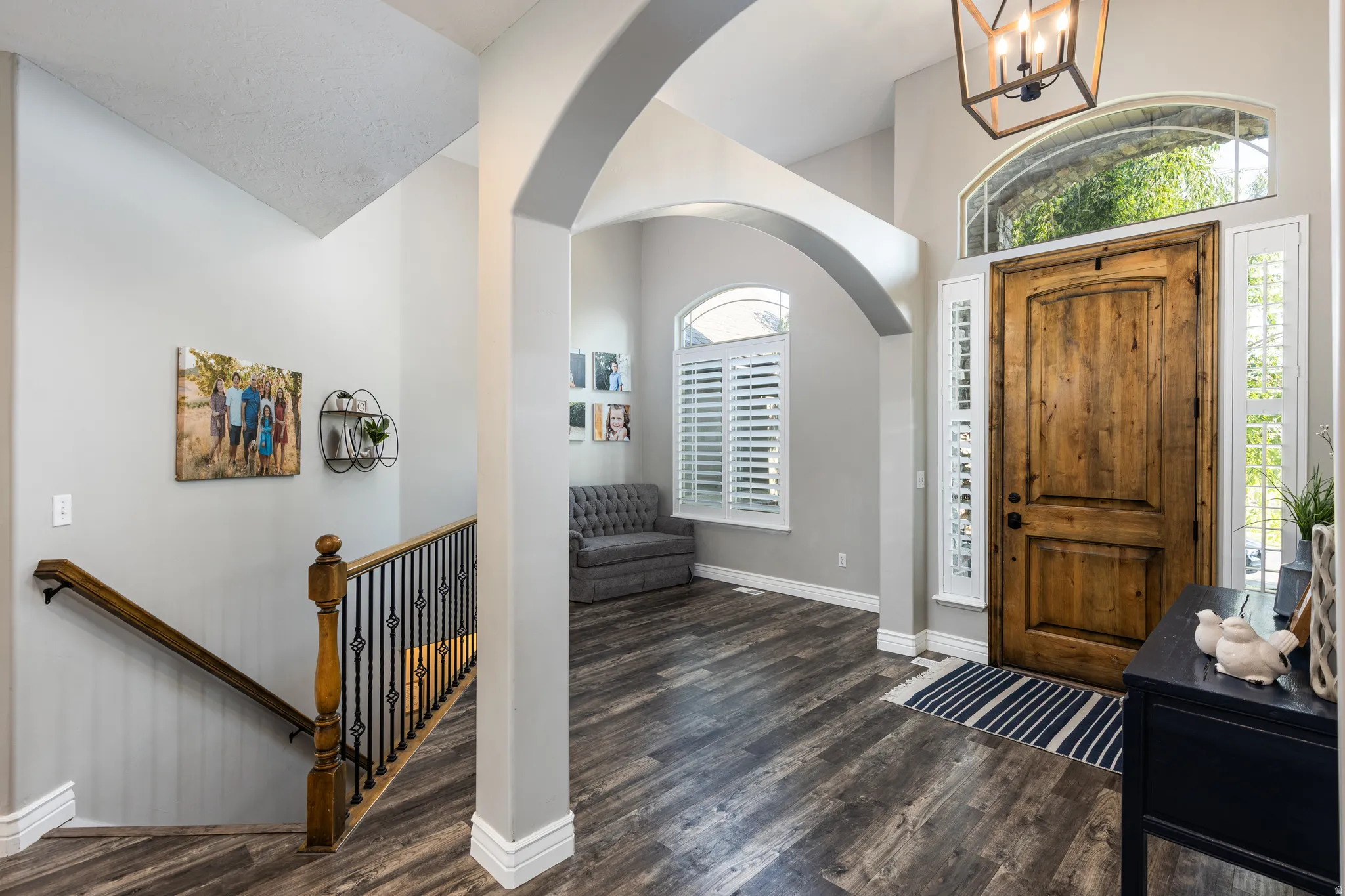 Welcoming foyer showcasing soaring ceilings with architectural arches, dark wood-finish flooring, and a curved staircase with wooden handrail and metal balustrade