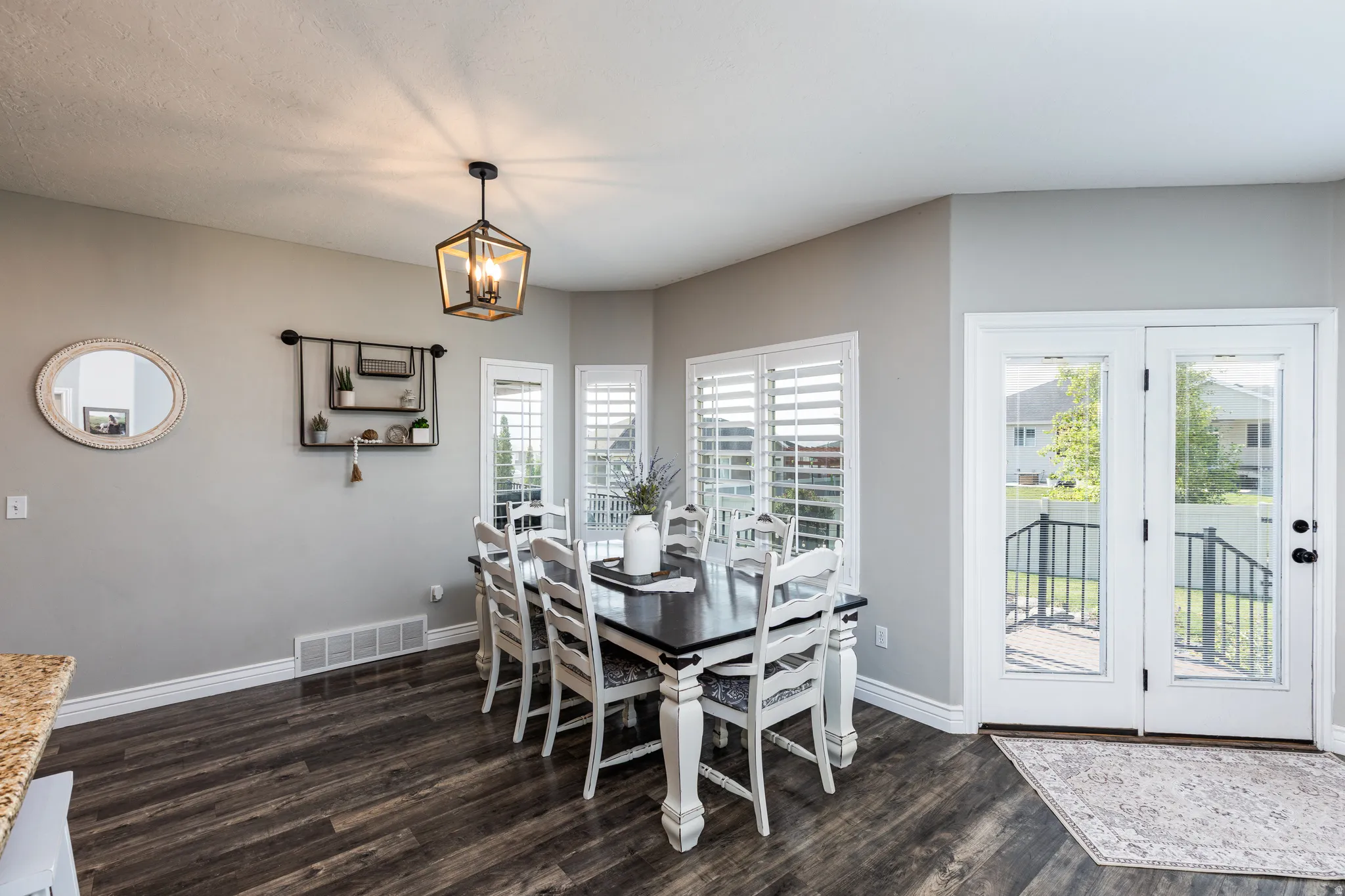 Dining room featuring a wood-finish plank floor, white painted dining table with matching chairs, and abundant natural light from dual glass doors opening to a covered deck