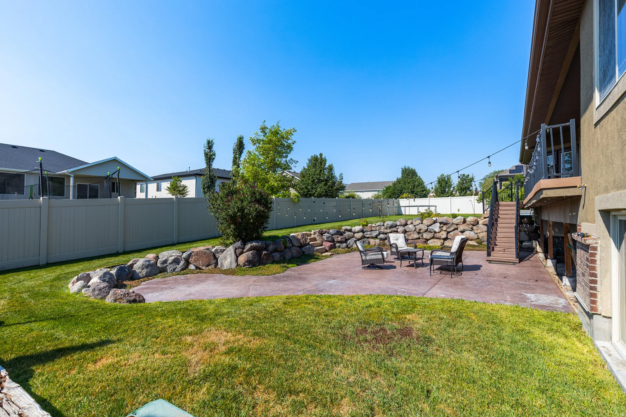 Expansive backyard featuring a stamped concrete patio, tiered rock landscaping, a privacy fence, and a wooden deck with stairs