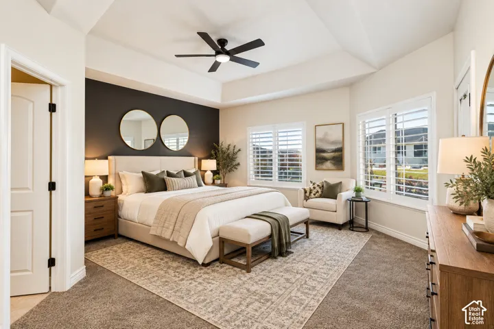 Tray ceiling with a black ceiling fan, two windows with white plantation shutters, and light wood-finish nightstands
