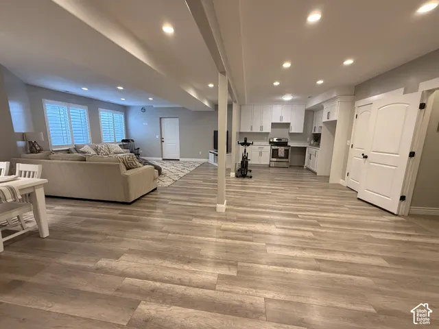 Recessed lighting illuminates the open-concept space featuring wood-finish flooring throughout, a full kitchen with white cabinetry, and two paneled doors