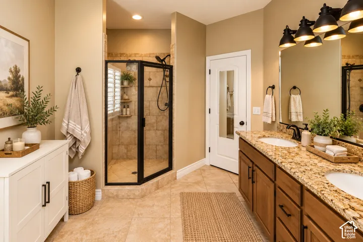 Dual sink vanity with stone-finish countertop, tiled walk-in shower with glass enclosure, tiled flooring, and recessed lighting