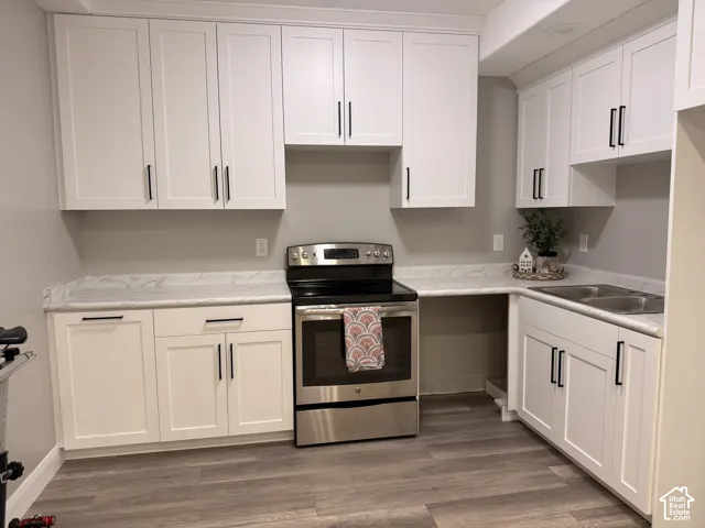 White shaker cabinetry with matte black hardware, stainless steel electric range, double basin stainless steel sink, wood-finish flooring, and light-toned countertops