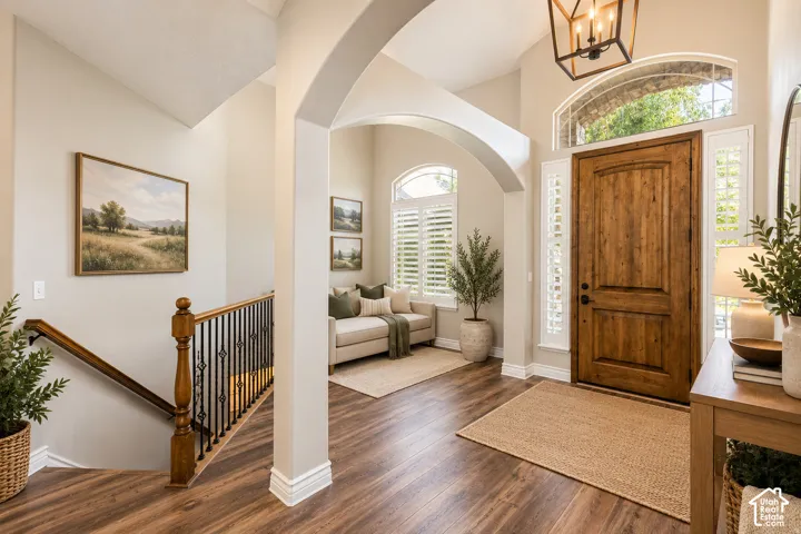 Wood-finish flooring throughout, arched entryway, wooden front door with transom window, plantation shutters, and a staircase with wood railing and metal spindles