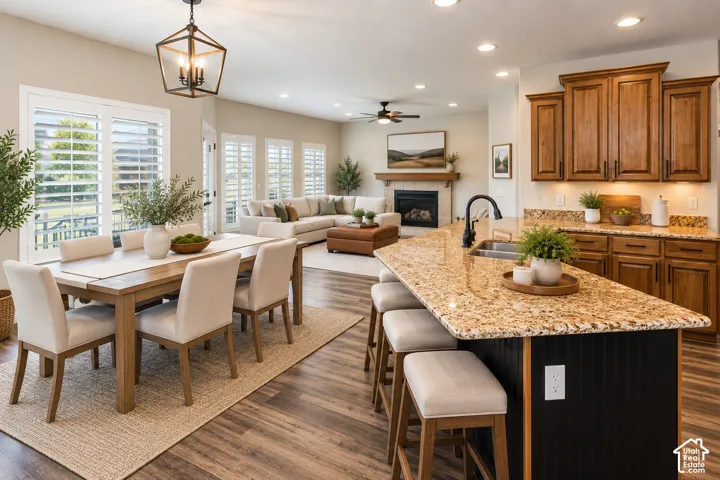 Open concept living area featuring wood-finish flooring throughout, a kitchen island with stone countertop and integrated sink, custom wood cabinetry, and a fireplace with a wood mantel