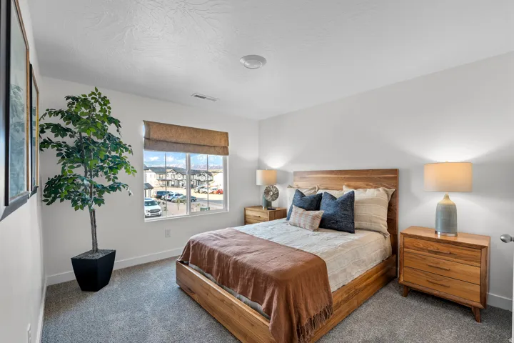 Carpeted bedroom featuring a large window with a Roman shade, light wood-finish flooring, and white walls