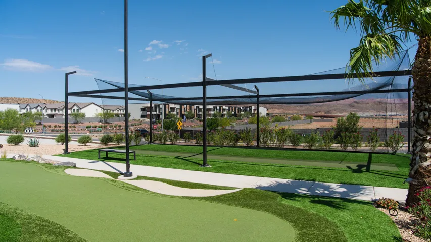 Putting green featuring artificial turf and a covered golf driving range