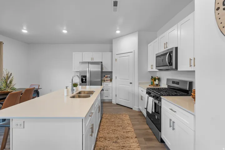 Modern kitchen featuring an expansive island with a double stainless steel sink, white shaker cabinetry, stainless steel appliances, and wood-finish flooring