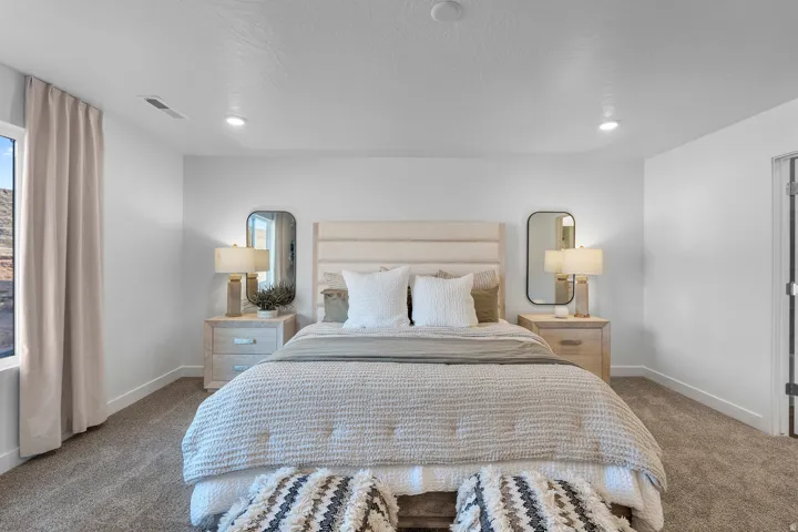 Well-lit bedroom featuring recessed ceiling lighting, a large window with neutral drapery, plush carpeting, and crisp white walls