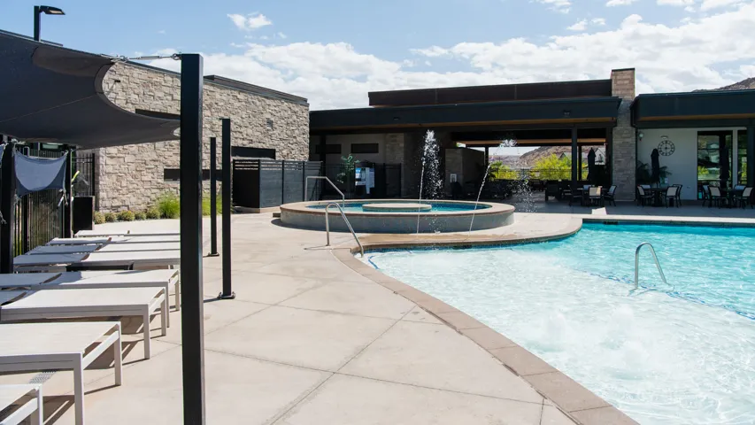Resort-style pool area featuring a large swimming pool, integrated spa with water features, and expansive concrete decking