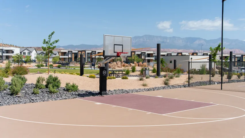 Outdoor half-basketball court with a tan and maroon playing surface, white court lines, and a black basketball hoop