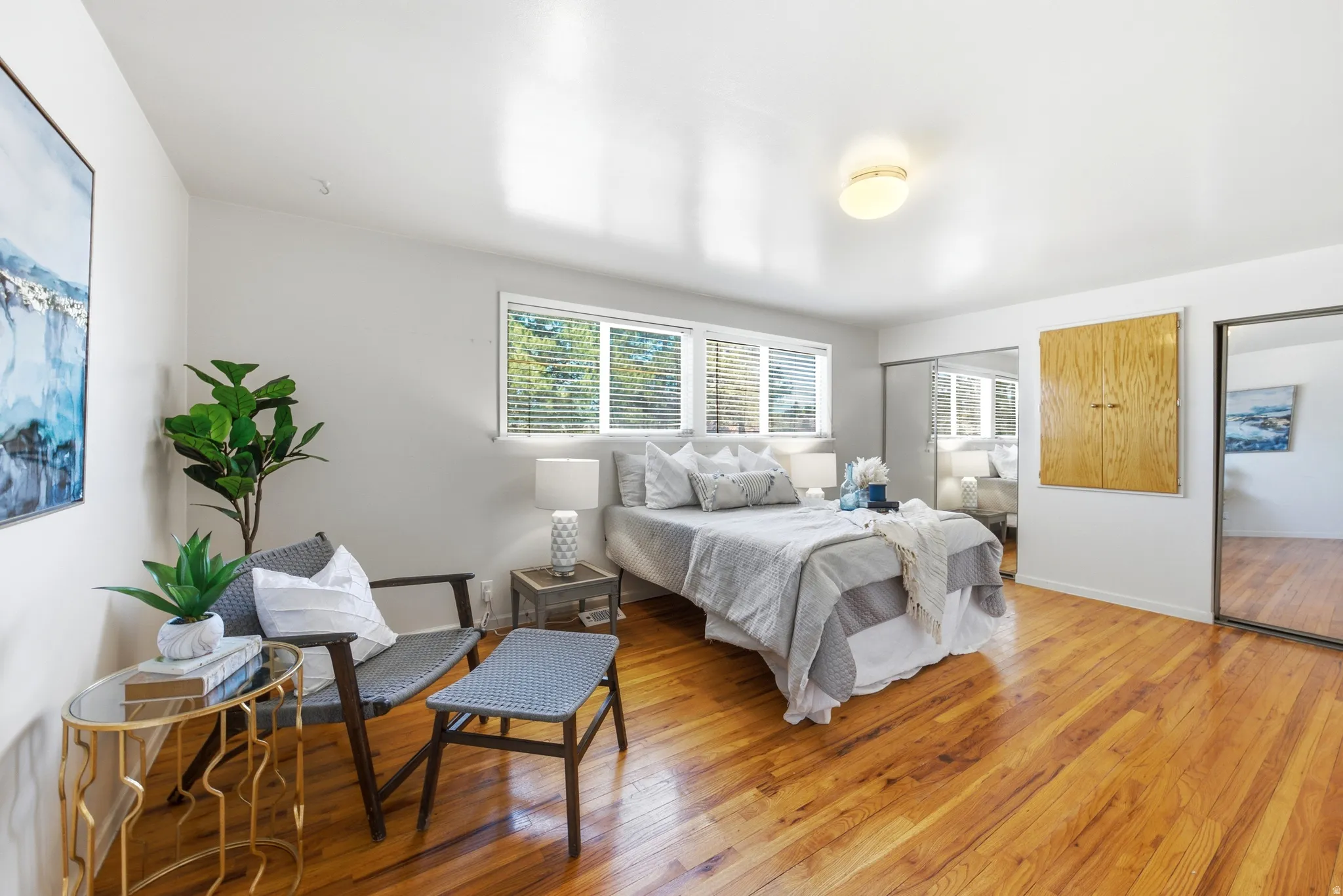 Hardwood-finish flooring throughout this room, featuring multiple windows with blinds, a built-in wooden cabinet, and sliding mirrored closet doors