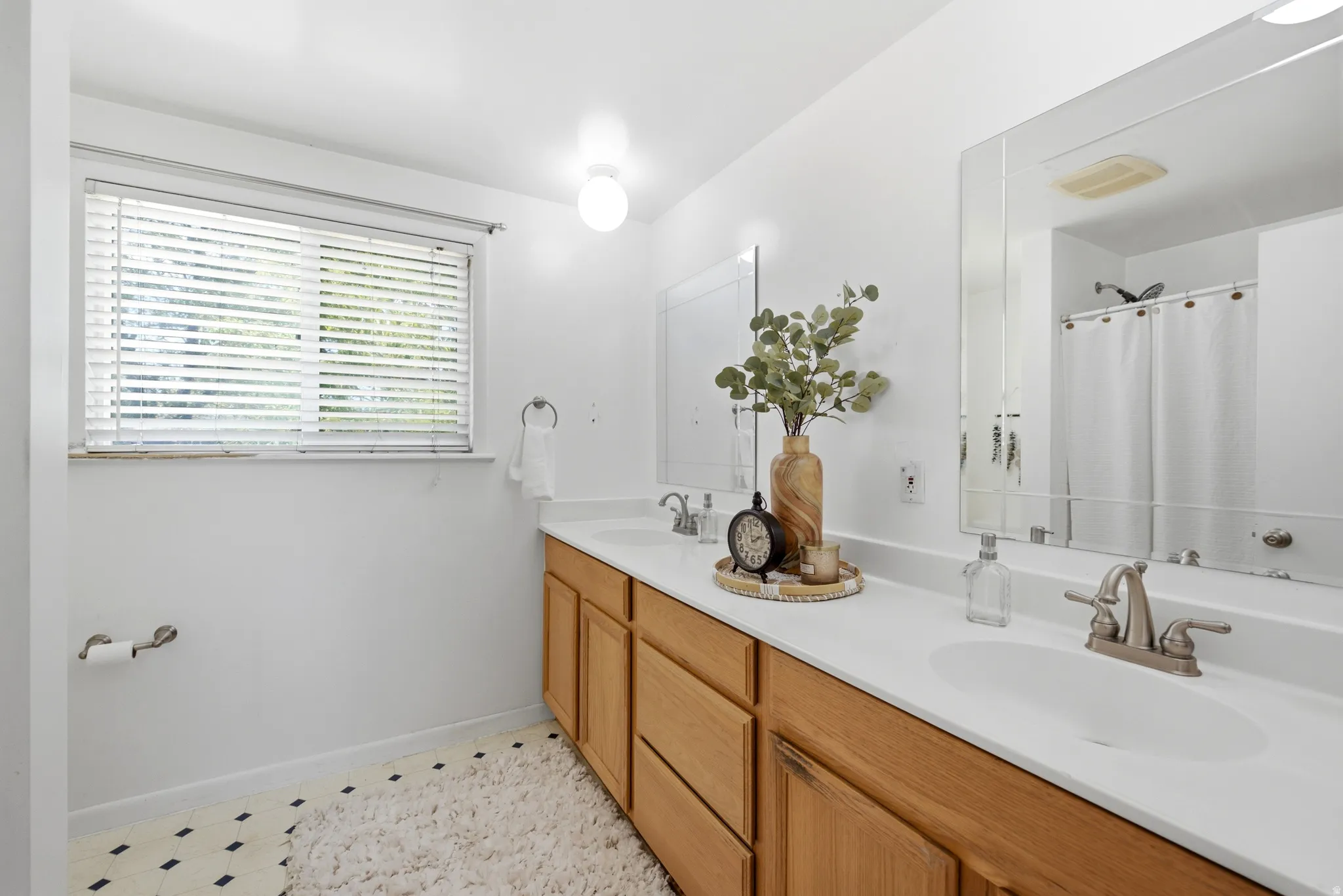 Double vanity with light wood-finish cabinetry, white countertops, and dual oval sinks