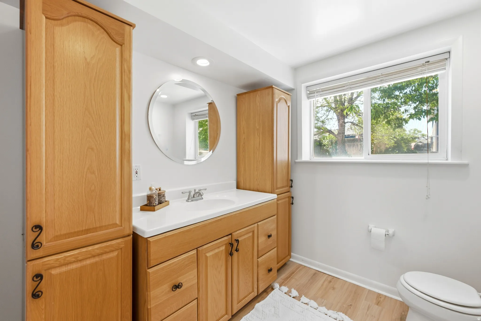 Bathroom featuring a wood-finish vanity with an integrated sink, a circular mirror, and recessed lighting