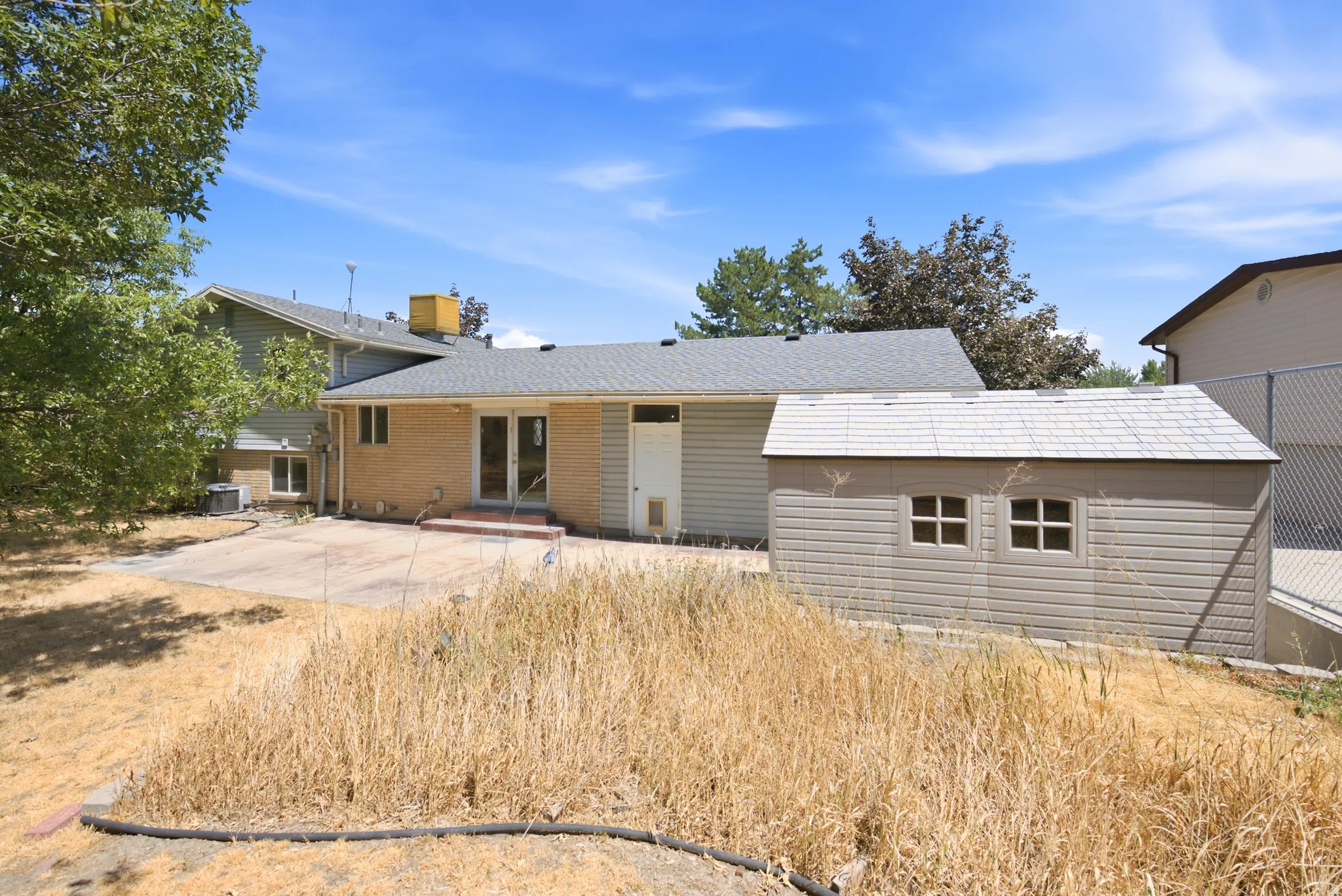 Rear exterior featuring a concrete patio, brick and siding facade, and a storage shed