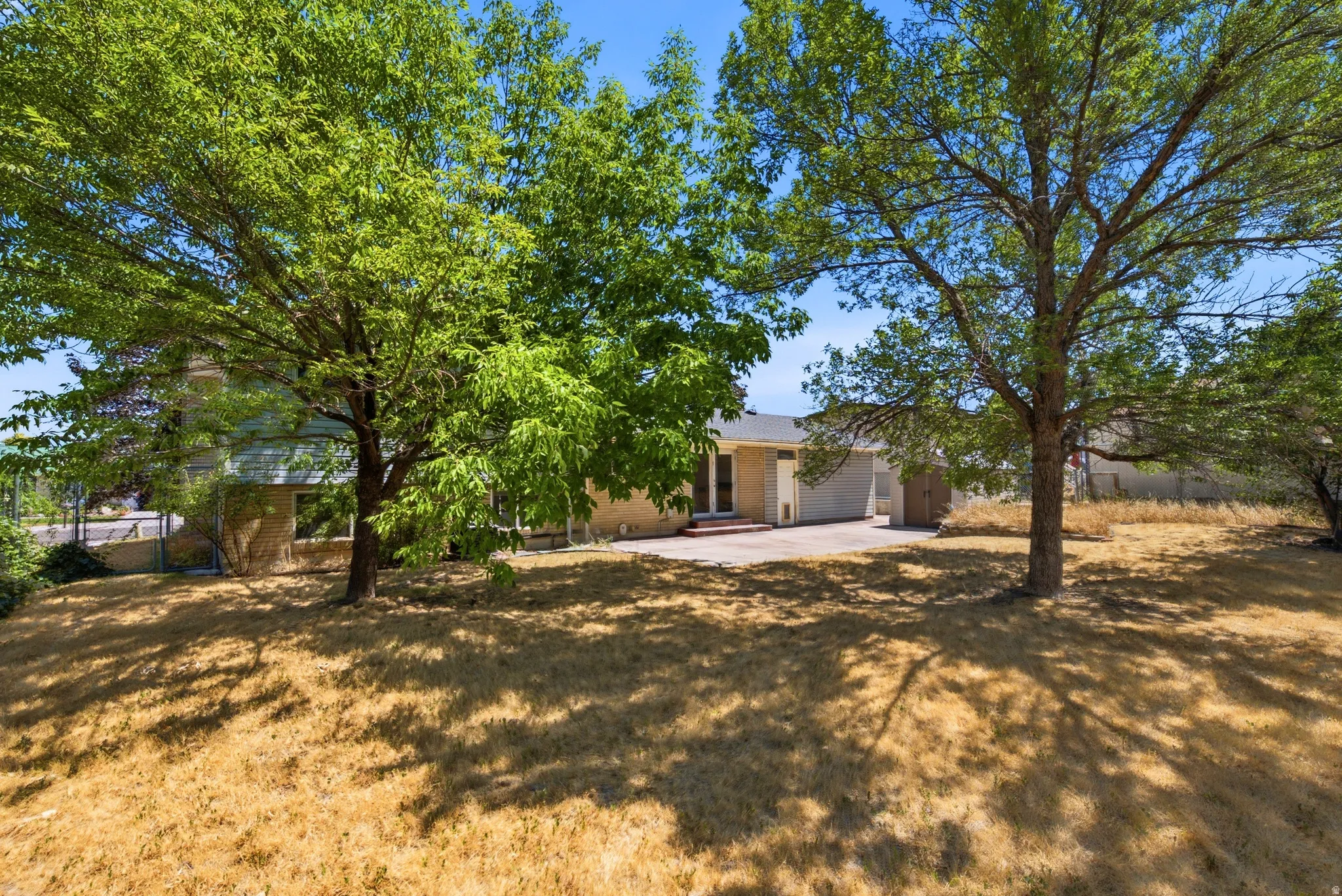 Expansive backyard featuring mature trees providing ample shade, a concrete patio, and exterior access to the property