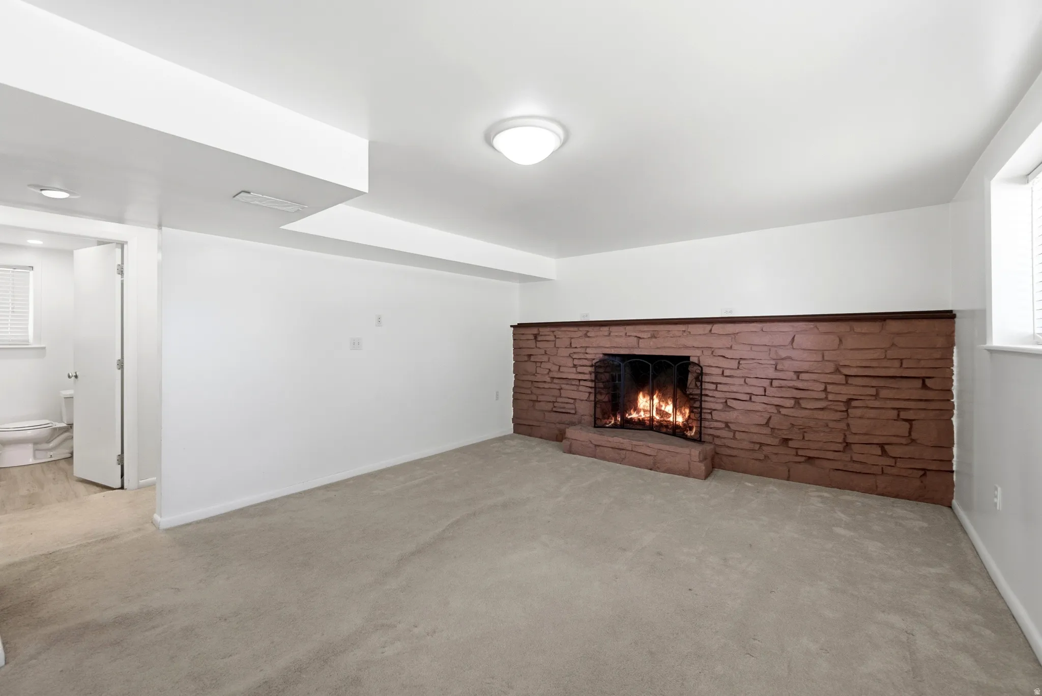 Carpeted room featuring a stone fireplace with a dark wood mantel and metal grate