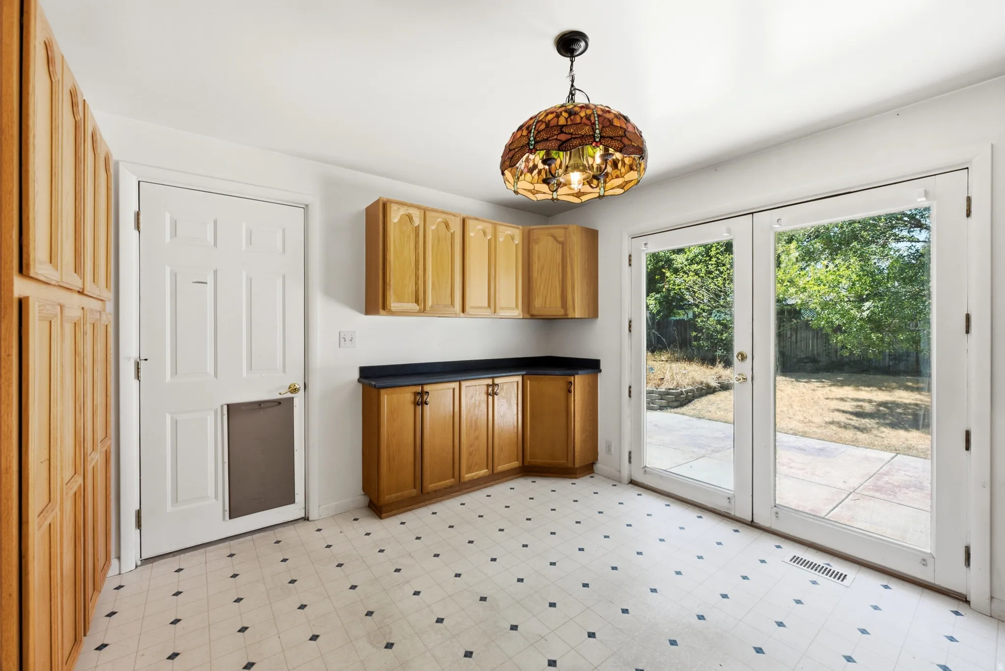Kitchen area featuring light wood cabinetry, black countertops, and patterned tile flooring