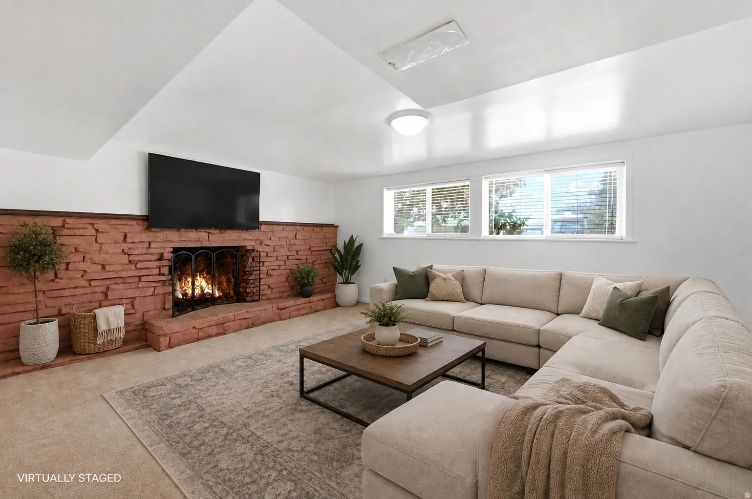 Living area featuring a floor-to-ceiling brick fireplace with a hearth, wall-mounted television, and two windows