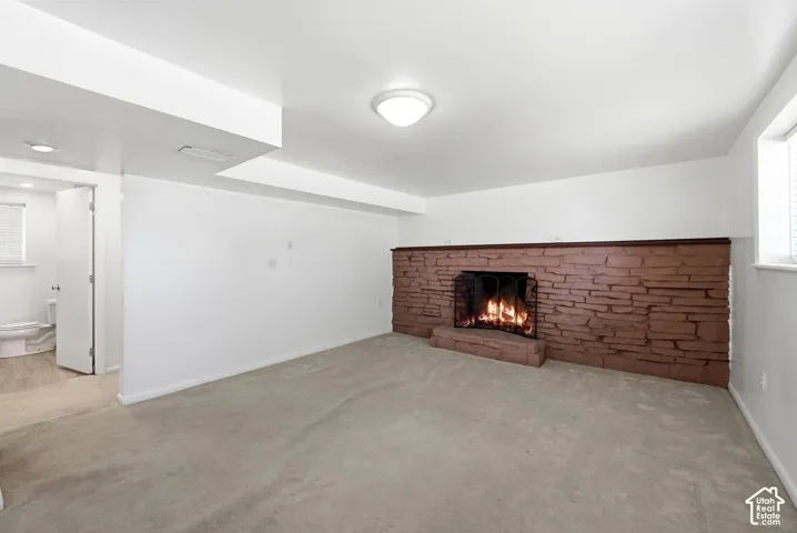 Carpeted room featuring a stone fireplace with a dark wood mantel and metal grate