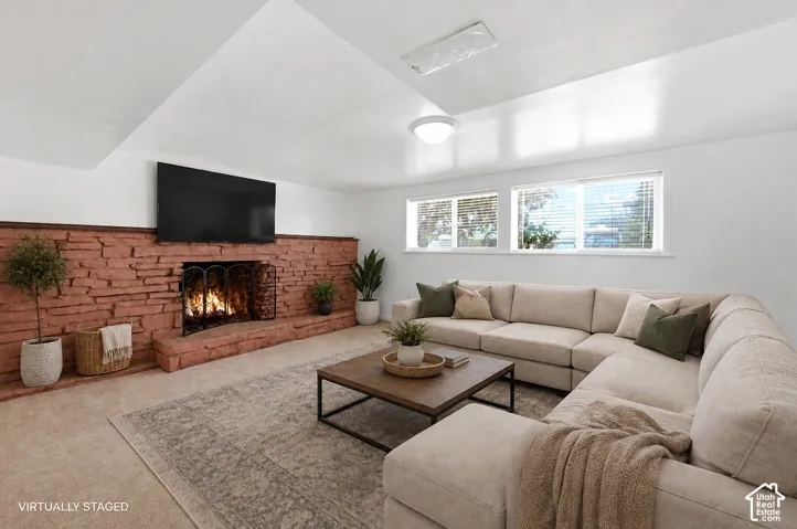 Living area featuring a floor-to-ceiling brick fireplace with a hearth, wall-mounted television, and two windows