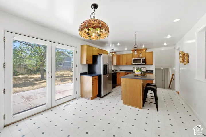 Kitchen featuring light wood cabinetry, a central island with a dark countertop, stainless steel appliances, and recessed lighting