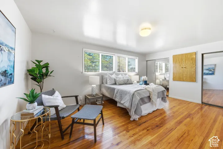 Hardwood-finish flooring throughout this room, featuring multiple windows with blinds, a built-in wooden cabinet, and sliding mirrored closet doors